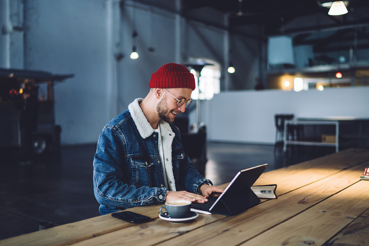 Person mit Laptop und Kaffee an langem Holztisch sitzend