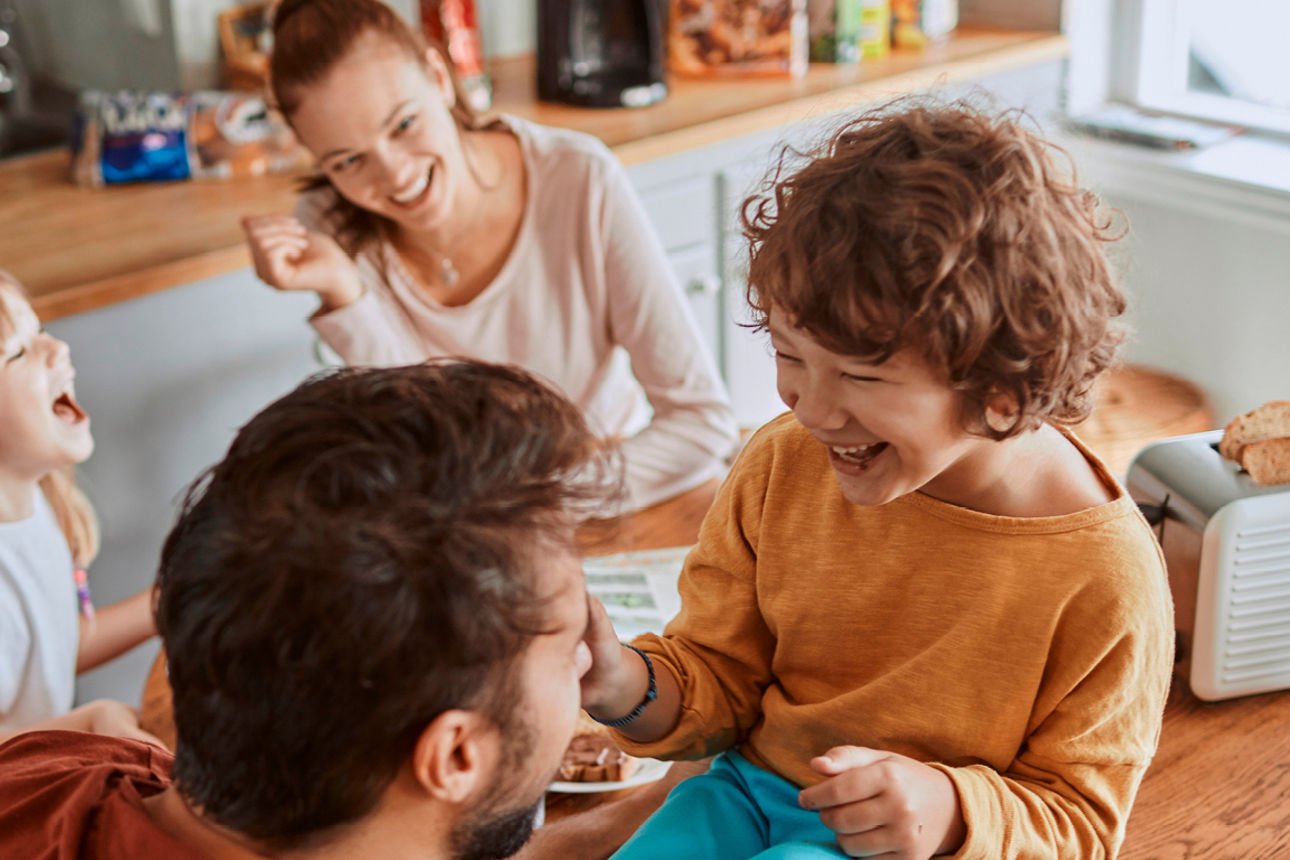 Mutter, Vater und zwei Kinder lachen zusammen am Frühstückstisch