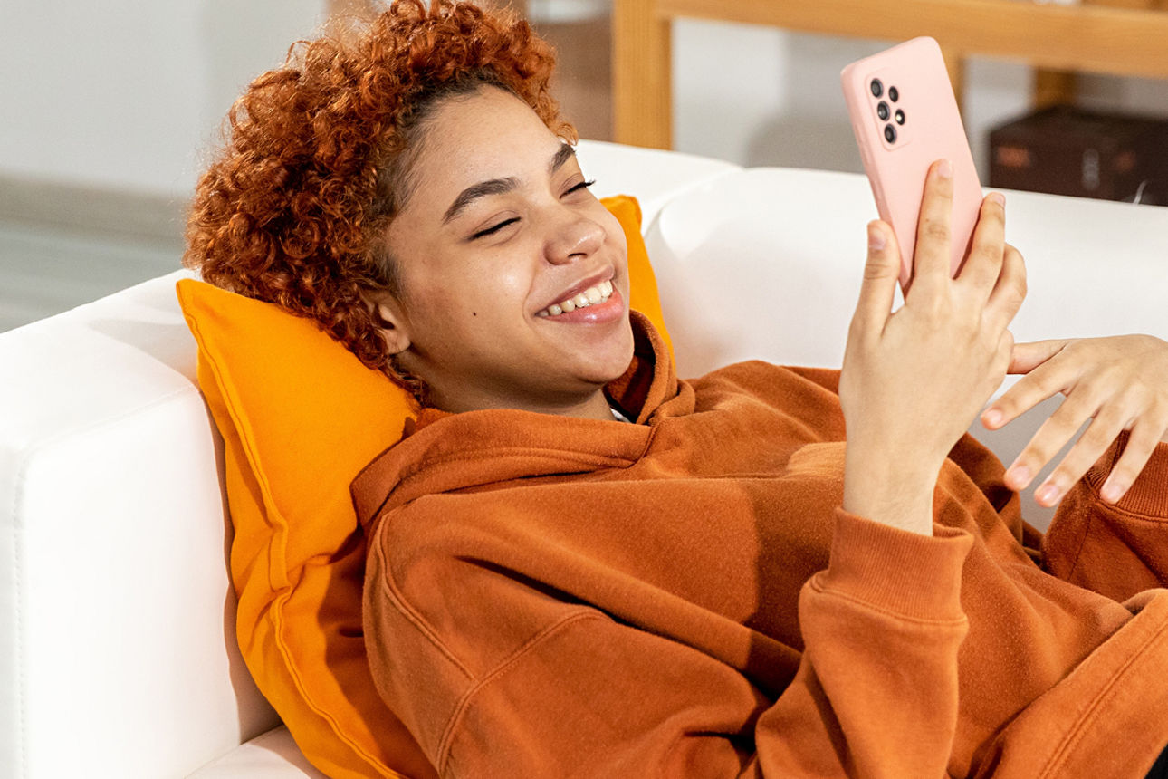 Junge Person liegt mit Handy auf einem Sofa