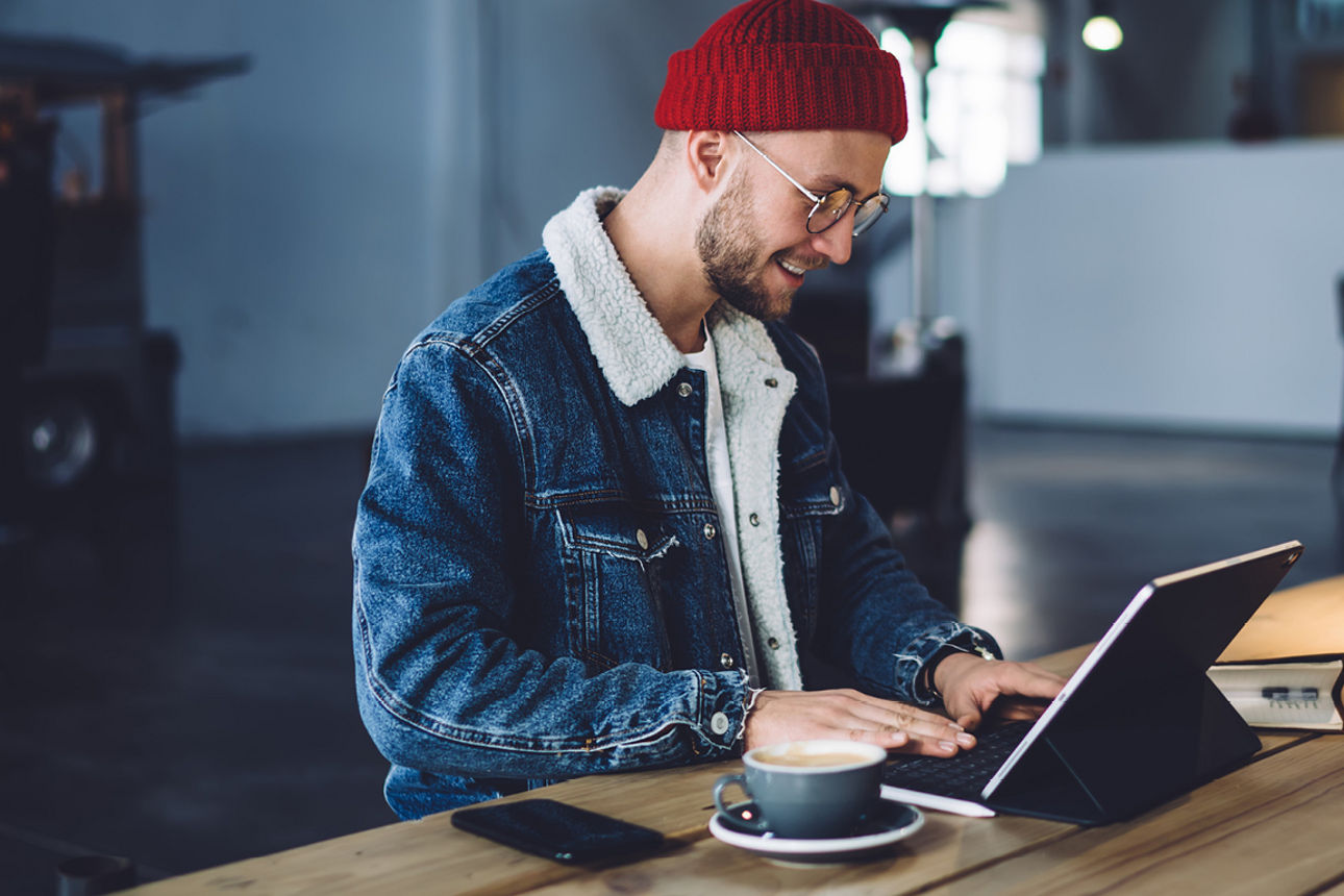 Person mit Laptop und Kaffee an langem Holztisch sitzend