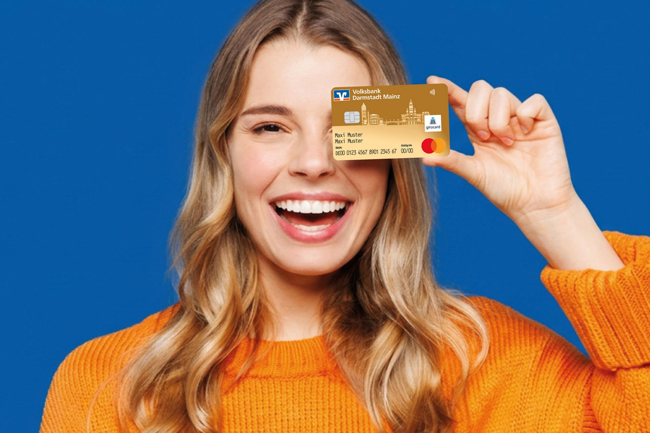 Glückliche Frau vor einer blauen Wand hält die girocard der Volksbank Darmstadt Mainz eG in der Hand