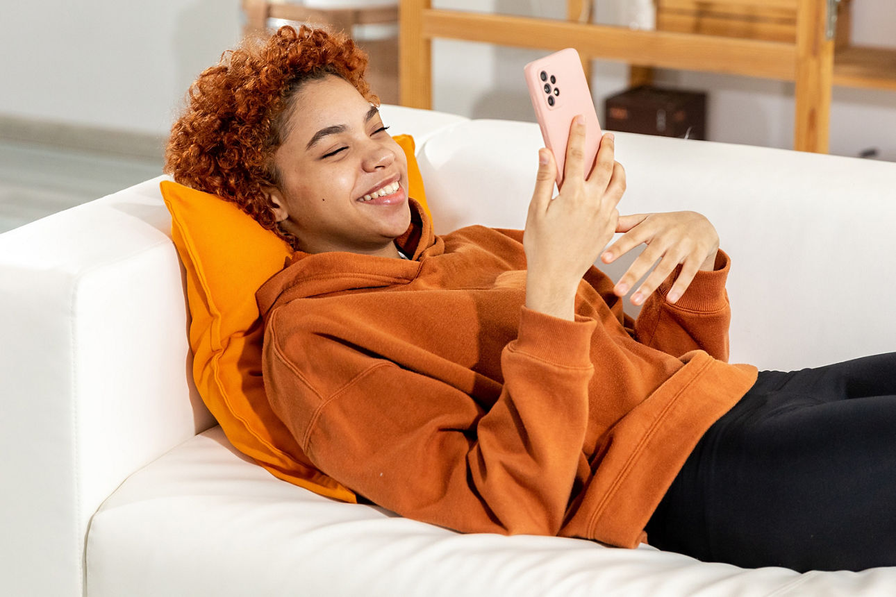 Jugendliche liegt mit dem Handy auf dem Sofa