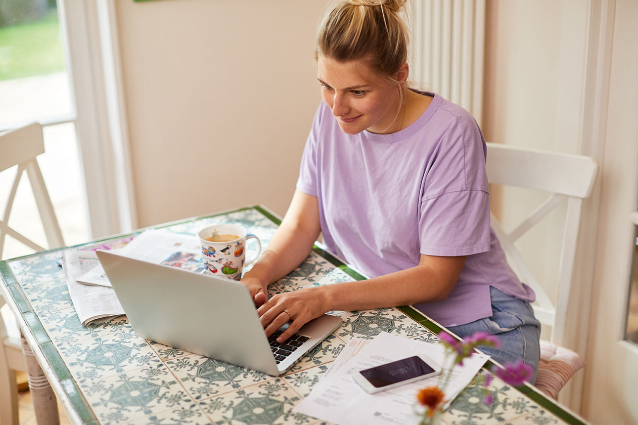 Frau sitzt am Tisch und arbeitet am Laptop