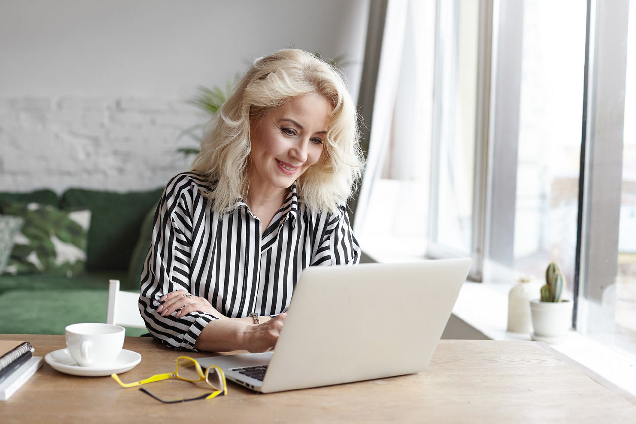 Frau sitzt am Tisch und arbeitet am Laptop.