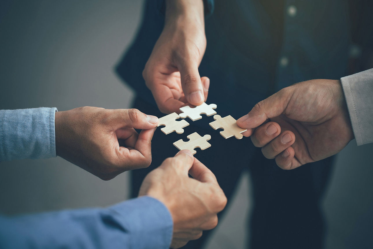 Vier Hände halten jeder ein Puzzleteil in der Hand
