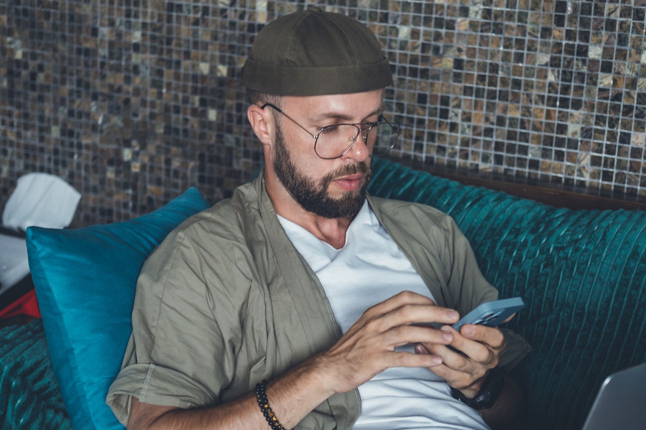 Junger Mann sitzt auf dem Sofa und sieht auf sein Handy
