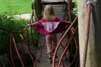 Ein Mädchen läuft auf einem Spielplatz über eine Hängebrücke