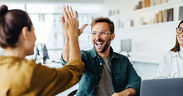 Junger Mann gibt einer jungen Frau ein High-Five, eine weitere Frau schaut lächelnd zu
