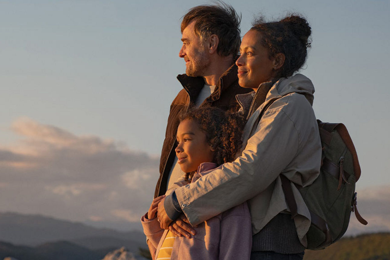 Eine Familie bei einer Wanderung in den Bergen schaut lächelnd dem Sonnenuntergang zu.
