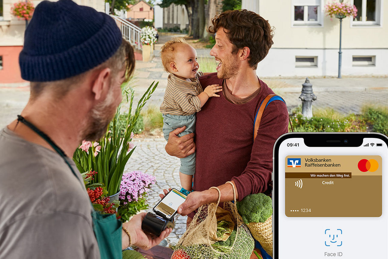 Mann mit Kind auf dem Arm bezahlt an Marktstand mit Apple Pay