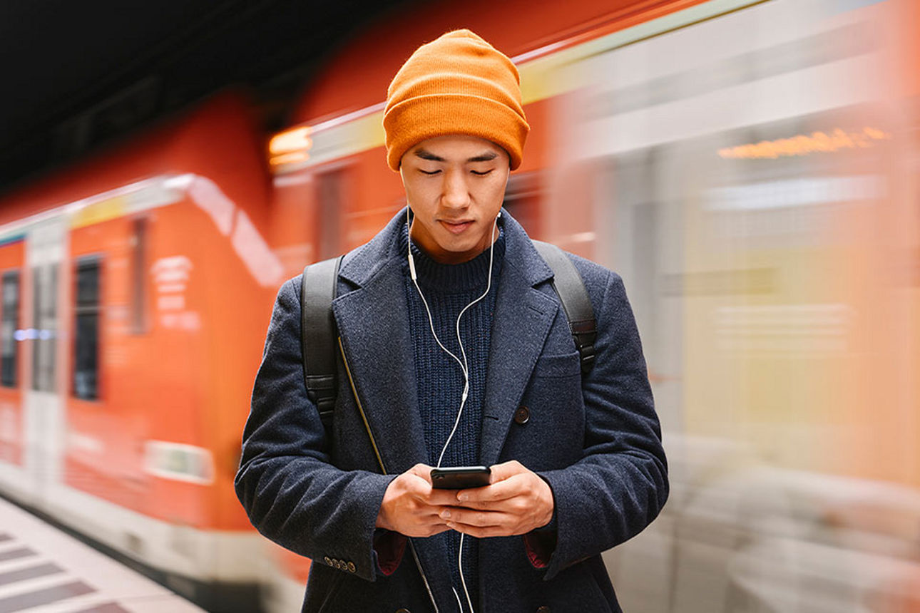 Mann in einer U-Bahn-Station, der auf sein Smartphone schaut