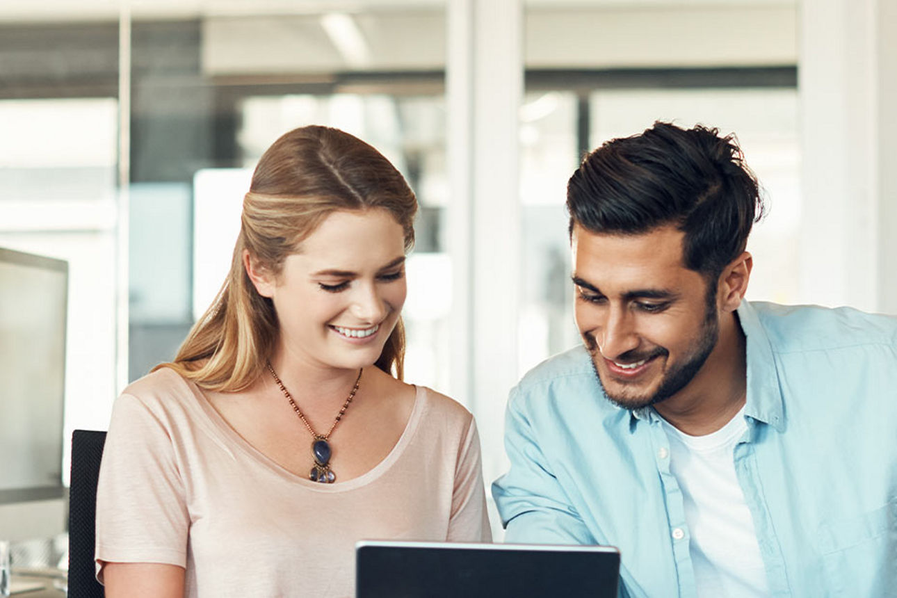 Eine Mann mit blauem Hemd und eine Frau schauen interessiert auf ein Laptop