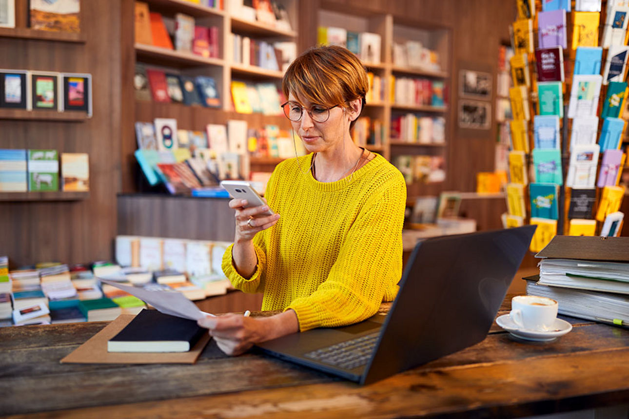 Mitarbeiterin in einer Buchhandlung schaut auf ihr Smartphone