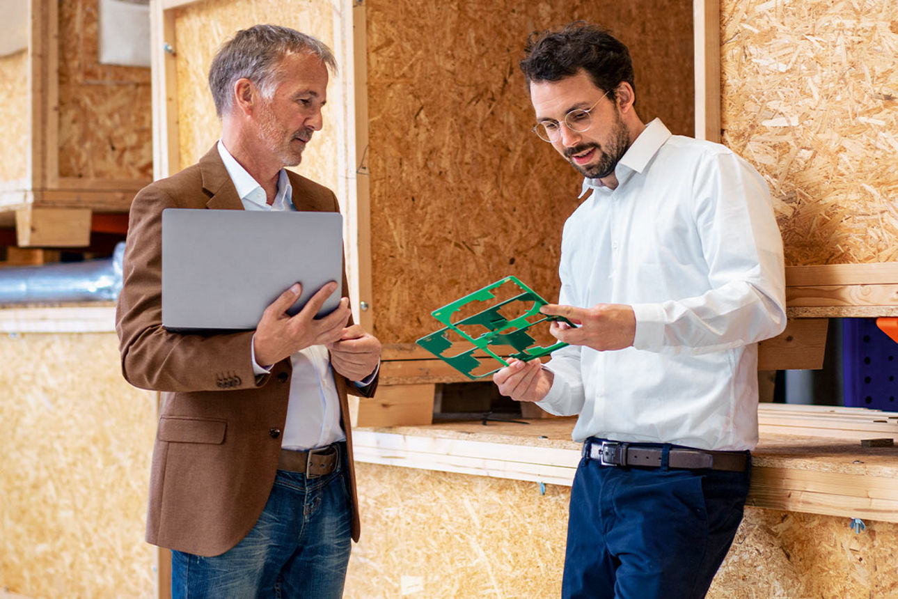 Zwei Männer sprechen in einer Werkstatt über Schablonen, die einer der beiden in der Hand hält.