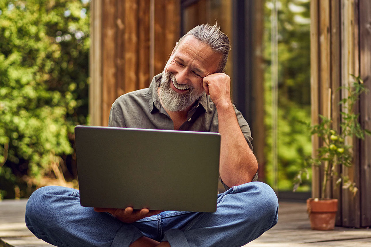 Mann sitzt mit Laptop auf der Terrasse