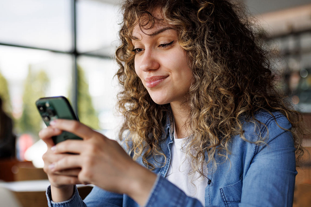Junge Frau sitzt im Café und hält ein Handy in der Hand