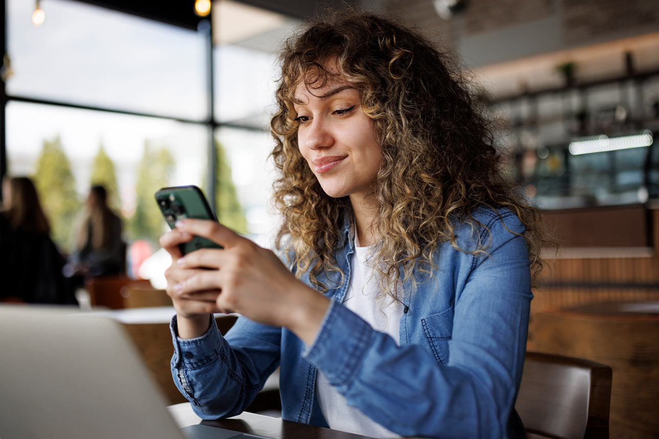 Junge Frau sitzt im Café und hält ein Handy in der Hand
