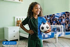 Mädchen steht mit Fußball in der Hand in einem Zimmer