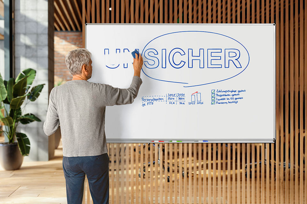 Mann steht vor einem Whiteboard mit der Aufschrift „Unsicher” und wischt die Vorsilbe „Un” weg