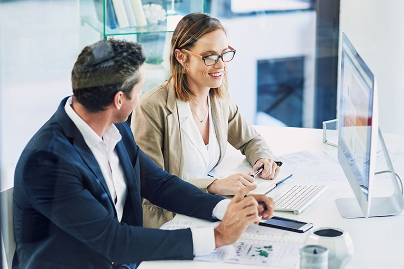 Ein Mann und eine Frau sitzen im Büro gemeinsam vor einen Bildschirm
